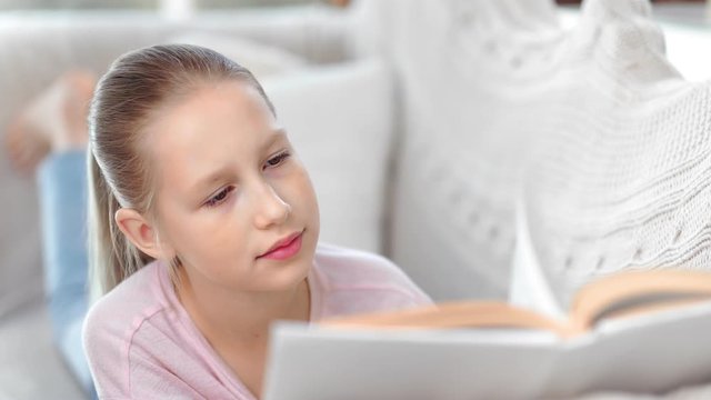 Close-up face cute child girl focused reading interesting book enjoying weekend at comfortable couch