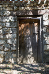 An old door with a rusty handle in a natural stone fence and a tiled roof. Treat sun falling through a big tree.