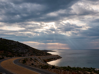 Sunbeams break through the clouds to the surface of the sea. Winding road in the morning