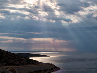 Sunbeams break through the clouds to the surface of the sea. Winding road in the morning