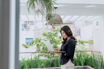 Trendy female business woman standing with laptop  in terrace outdoor. Student girl reading a presentation on laptop. education, lifestyle and people concept.