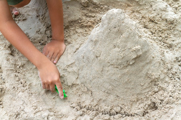 Close up children's hands holding green toy tools playing pile sand on the beach background. Selective focus at the right hand.