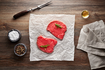 Slices of raw veal beefsteak on white cooking paper and wooden table