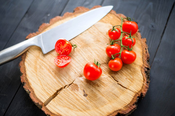 Knife and fresh cherry tomatoes on a wooden board, closeup.