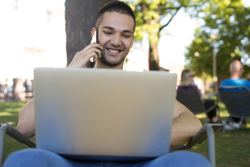 Cheerful man smart university student talking via smartphone during online education via notebook...