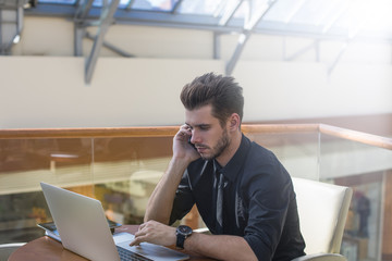Business man talking with partner via mobile phone while sitting with laptop computer inside company 