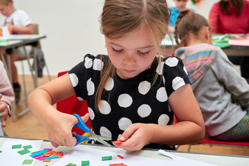 A childrens craft session in front of a teacher cutting up colourful paper with scissors