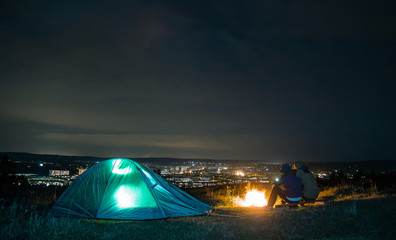 Fototapeta na wymiar loving couple at night near the fire. couple watching the city at night. beautiful night vision scenery. campfire around people, be near the fire, the concept of relaxation