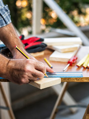 Adult craftsman carpenter with pencil and ruler tracing the cutting line on a wooden table. Housework, do it yourself. Stock photography.