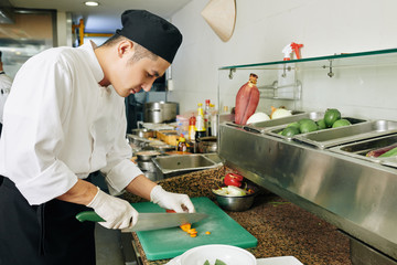 Asian young chef cutting the carrot with knife on cutting board in the kitchen of the restaurant