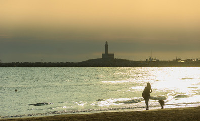 Gargano coast: bay of Vieste, (Apulia) Italy. Girl with dog walking on the  sandy beach at dawn:in...