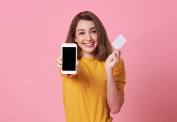 Portrait of a happy young woman showing at blank screen mobile phone and credit card isolated over...
