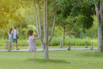 Fototapeta premium A little girl in a pink skirt enjoys a relaxing time playing on the green lawn at the public park in the evening.