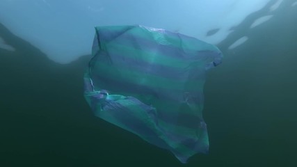 Plastic pollution, striped blue bag swims underwater surface in sunray on background blue sky with clouds. Low-angle shot. Plastic debris underwater. Plastic garbage environmental pollution problem 