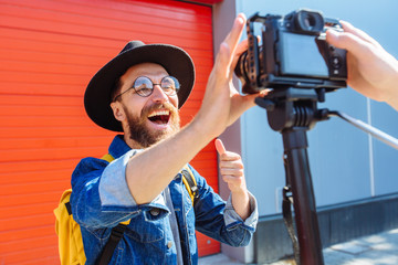 social media influencer creating content. man shooting video of himself using camera on tripod. smiling bearded hipster guy communicating with subscribers. - obrazy, fototapety, plakaty