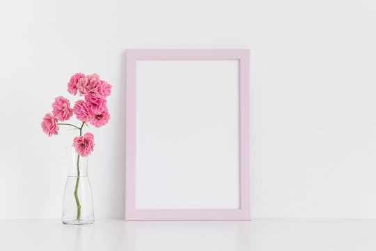 Pink frame mockup with pink roses in a glass vase on a white table.Portrait orientation.