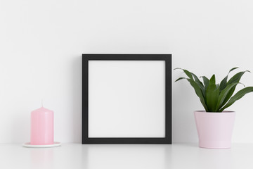 Black square frame mockup with a dracaena in a pot and a candle on a white table.