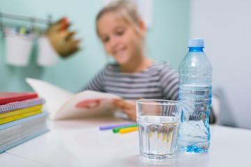 close up of glass of water, blurred schoolgirl doing home work in her room