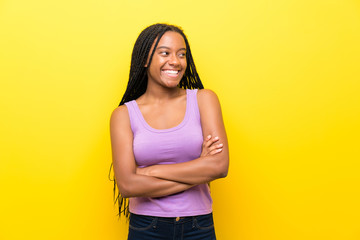 African American teenager girl with long braided hair over isolated yellow wall happy and smiling