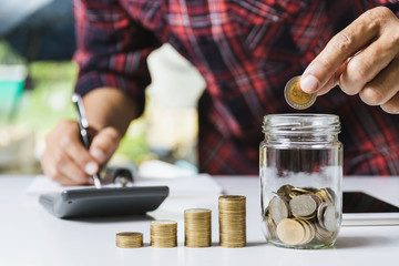 Men are Saint documents about save money and put coin in glass jar also have  calculator, coins on desk