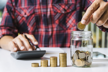 Men are Saint documents about save money and put coin in glass jar also have  calculator, coins on desk