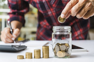 Men are Saint documents about save money and put coin in glass jar also have  calculator, coins on desk