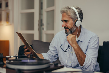 middle aged man sitting sofa and listening music on record player in his home