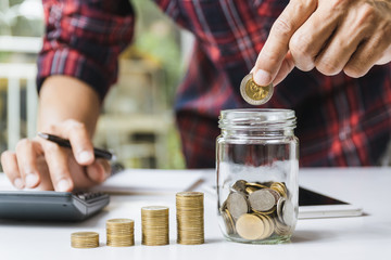 Men are Saint documents about save money and put coin in glass jar also have  calculator, coins on desk
