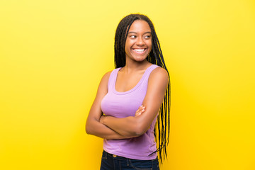 Obraz premium African American teenager girl with long braided hair over isolated yellow wall with arms crossed and happy