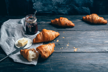 croissants, plum jam and butter on dark wooden table with copyspace