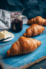 tasty croissants, butter and plum jam on blue wooden table