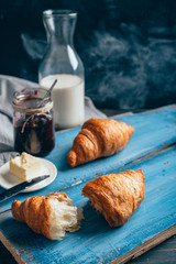 tasty croissants, butter and milk on blue wooden table