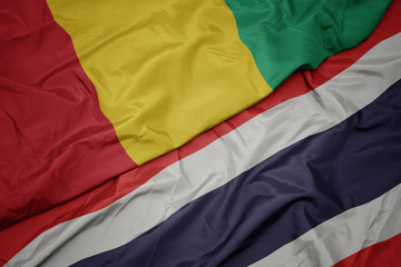 waving colorful flag of thailand and national flag of guinea.