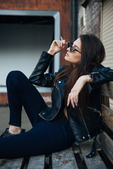 Fototapeta na wymiar young girl in a leather jacket smokes cigarettes, rock style, cheeky and cute girl street posing style, rock punk lifestyle
