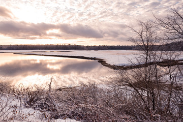 Winter landscape. A lake among a snowy field and forest at sunset. USA. Maine