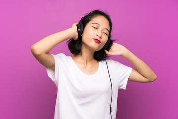 Asian young girl listening music with a mobile and dancing over isolated purple wall