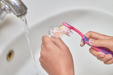 A girl brushes a removable orthodontic appliance. Concept of pediatric dentistry, correcting the bite. Closeup, selective focus