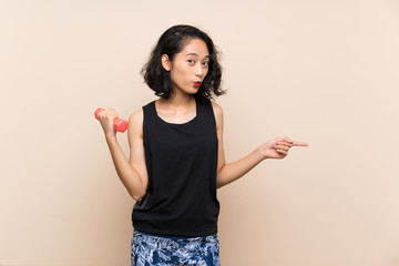 Young Asian girl making weightlifting over isolated background surprised and pointing side