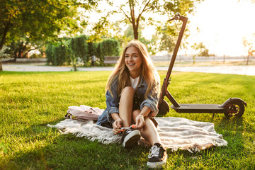 Positive young teenage girl sit outside in nature green park on grass with scooter. © Drobot Dean
