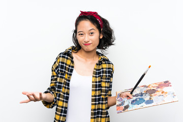 Young artist woman holding a palette over isolated white background making doubts gesture while...