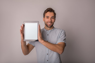 Portrait of a happy smiling handsome bearded man holding portable touch pad computer with empty mock up copy space screen background for promotional content, standing isolated in studio