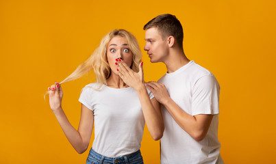 Guy whispering secret or gossip to surprised girl - obrazy, fototapety, plakaty