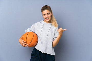 Teenager girl playing basketball over grey wall with thumbs up because something good has happened