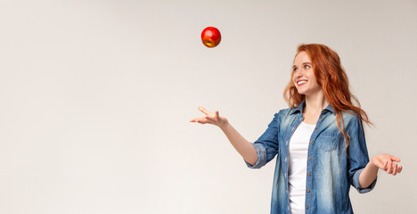 Beautiful redhead girl throwing apple in the air