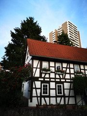 Altes Fachwerkhaus mit Spitzgiebel und modernes Hochhaus mit Wohnungen und Apartments vor blauem...