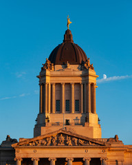 Closeup of the Manitoba Legislative Building with the "Golden Boy" statue on top, shot during golden hour. (Moon visible in the background) - Winnipeg, Manitoba/Canada