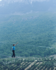 A man is walking along a stretched sling. Highline in the mountains. Man catches balance. Performance of a tightrope walker in nature. Highliner on the background of the mountains.