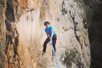 A man is walking along a stretched sling. Highline in the mountains. Man catches balance. Performance of a tightrope walker in nature. Highliner on the background of the mountains.