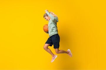 Fototapeta na wymiar Teenager girl basketball ball jumping over isolated yellow background.