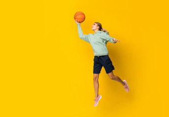 Teenager girl basketball ball jumping over isolated yellow background.